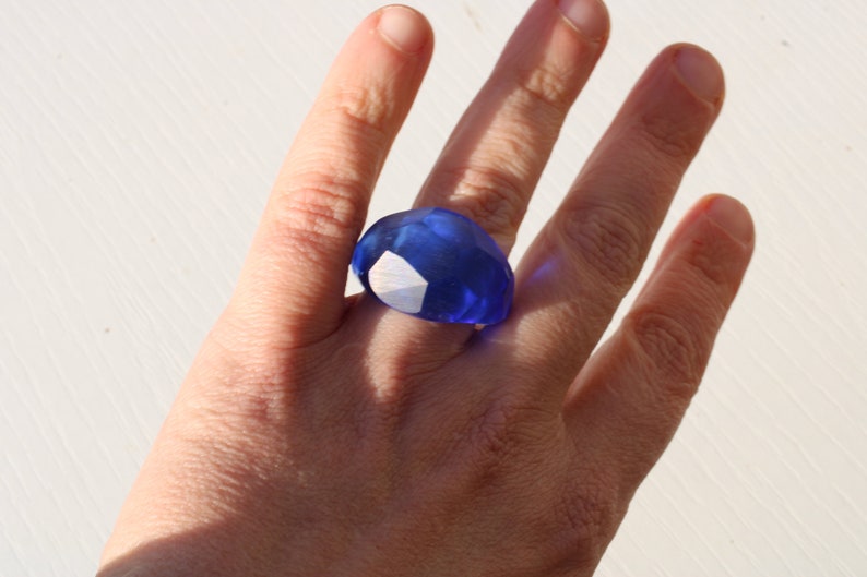 May include: A large, blue, faceted ring worn on a finger.