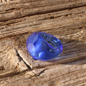 May include: A blue glass ring with a faceted design. The ring is sitting on a piece of weathered wood.