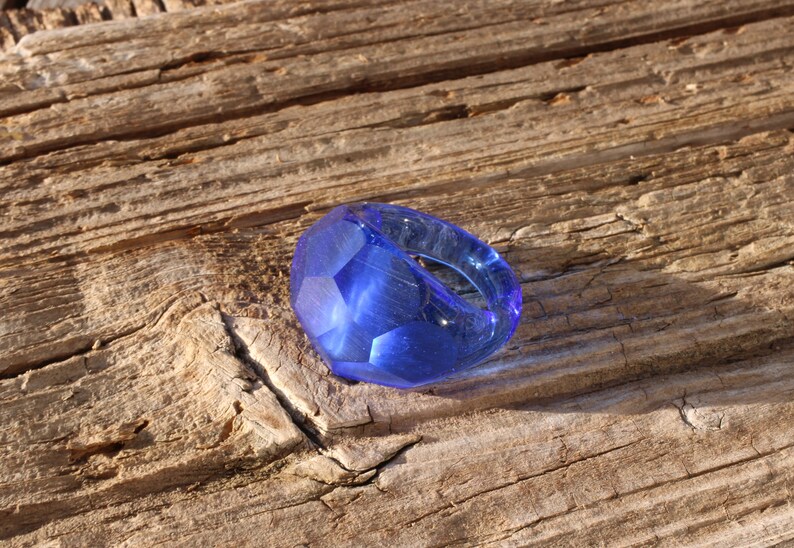 May include: A blue glass ring with a faceted design. The ring is sitting on a piece of weathered wood.