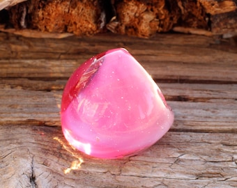 May include: A pink glass paperweight with a white swirl inside. The paperweight is sitting on a piece of weathered wood.