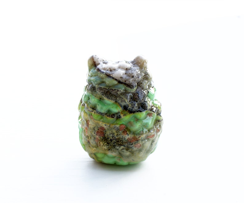May include: A small, green, and brown ceramic owl figurine with a textured surface.