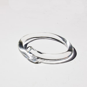 May include: A clear glass bangle bracelet with a unique, twisted design.