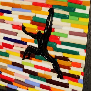 K&ouml;nnte beinhalten: Eine schwarze Glasskulptur einer Person, die eine Wand aus bunten Glasfliesen erklimmt.