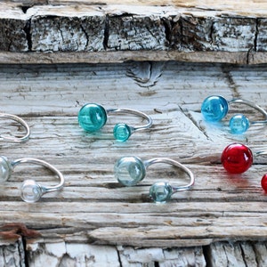 May include: A set of eight silver rings, each featuring two glass spheres. The spheres come in a variety of colours, including clear, yellow, blue, green, and red.