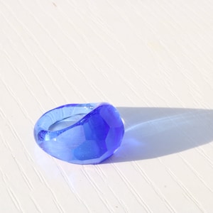 May include: A blue glass ring with a faceted design. The ring is made of clear glass with a blue tint.