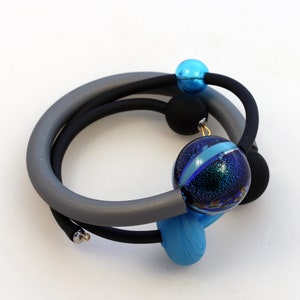 May include: A gray and black bracelet with blue and iridescent glass beads. The bracelet is made of two different types of cord, one gray and one black. The beads are all different shapes and sizes.