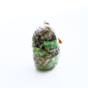 May include: A green, brown, and white owl figurine with a small orange beak. The owl is made of glass and has a textured surface.