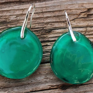 May include: A pair of silver hoop earrings with round, green glass pendants. The glass is translucent and has a slight shimmer.