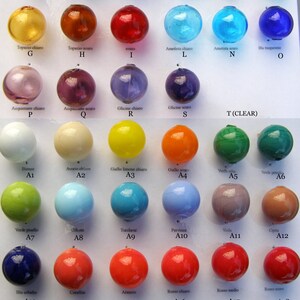 May include: A chart with 20 glass beads in different colors and shades. The beads are labeled with Italian names for the colors, such as "rosso" for red, "bluino" for blue, and "verde" for green. The beads are arranged in rows and columns, and each bead is labeled with a letter and number.