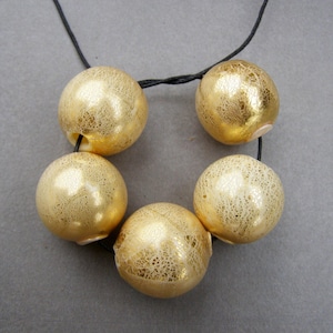 May include: A necklace featuring five gold-coloured beads, each with a textured surface. The beads are strung on a black cord.