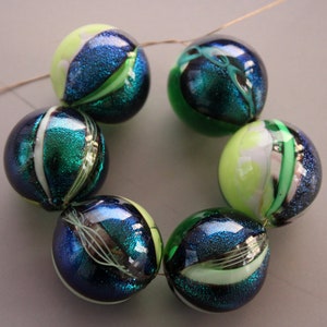 May include: A strand of six glass beads with a green, blue, and white swirl pattern. The beads are strung on a wire and are arranged in a circle.
