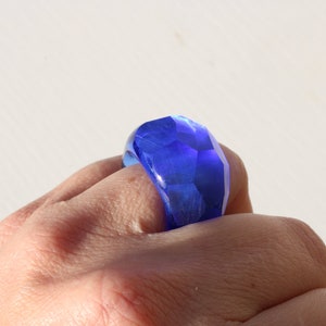 May include: A blue faceted glass ring worn on a finger.