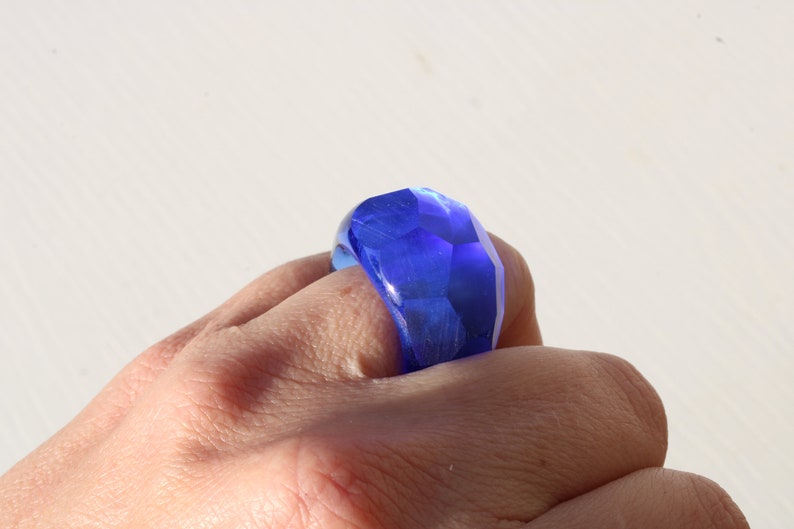 May include: A blue faceted glass ring worn on a finger.