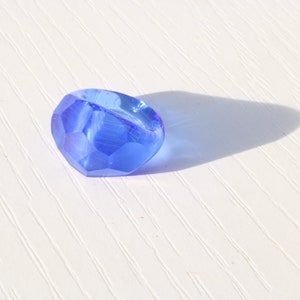 May include: A single, faceted, blue glass bead. The bead is round and has a smooth, shiny surface.