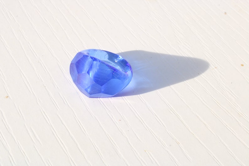 May include: A single, faceted, blue glass bead. The bead is round and has a smooth, shiny surface.