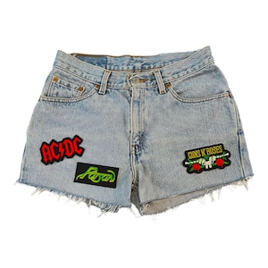 May include: Light blue denim shorts with frayed edges and three band patches. The patches are red and black with the text "AC/DC", green with the text "Poison", and gold with the text "Guns N' Roses".