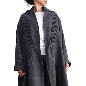 May include: A long, dark blue linen coat with a relaxed fit and pleats on the front. The coat has a collar and long sleeves.