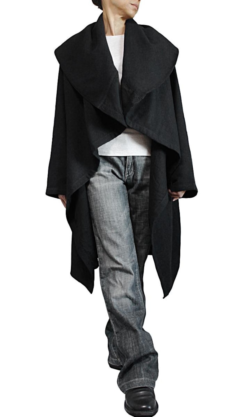 May include: A black, draped coat with a wide collar. The coat is worn over a white shirt and blue jeans. The coat has long sleeves and a flowing design. The person is wearing black shoes.