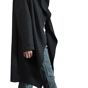 May include: A long, black hooded coat with a draped design. The coat features a large hood and a button closure. The person is wearing blue jeans and black shoes. The coat is made of a soft, flowing fabric.
