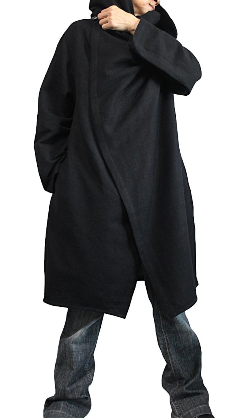 May include: A long, black coat with a hood. The coat has a wrap-style design and is worn with blue jeans. The coat appears to be made of a heavy fabric, suitable for cooler weather. The overall style is minimalist and modern.