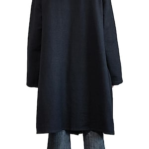 May include: A long, black hooded coat with long sleeves. The coat is made of a soft, dark fabric and reaches to the mid-calf. The person is wearing blue jeans. The background is white.