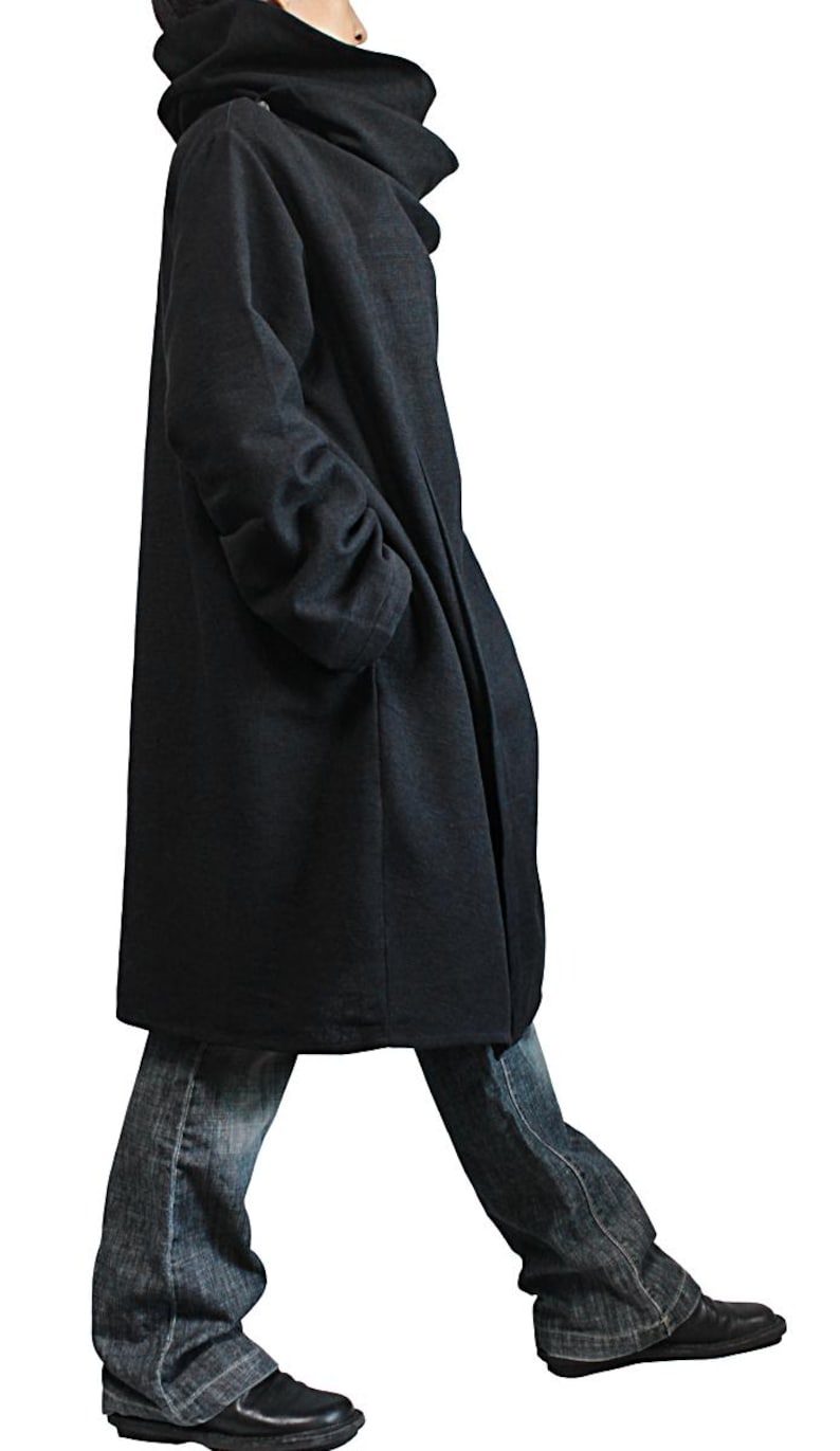 May include: A dark gray hooded coat with a high collar and long sleeves. The coat is knee-length and worn with blue jeans and black shoes. The coat has a relaxed fit and a minimalist design, suitable for casual wear.