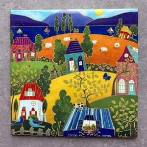 May include: Square ceramic tile with a vibrant village scene. The artwork shows houses with red, blue, and purple roofs, set against a yellow and orange landscape. Trees, sheep, and sailboats are also depicted.