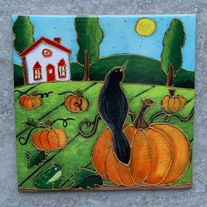 May include: A square ceramic tile depicting an autumnal scene. A black crow sits on a large orange pumpkin in a field of pumpkins. A white house with a red roof is on a green hill under a blue sky with a yellow moon.