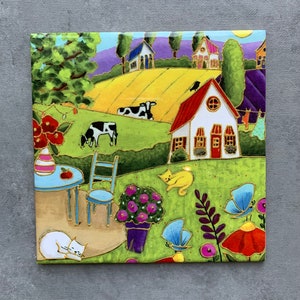 May include: A colorful illustration of a countryside scene with a white house, a yellow cat, two cows, a blue table and chairs, and a flower pot with purple flowers. The background features a rolling green hill with a yellow field and a blue sky.