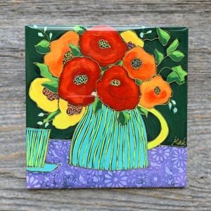 May include: A square decorative tile featuring a painting of a turquoise striped pitcher filled with vibrant red, orange, and yellow flowers against a dark green background, set upon a purple surface with a floral pattern and a small matching cup.
