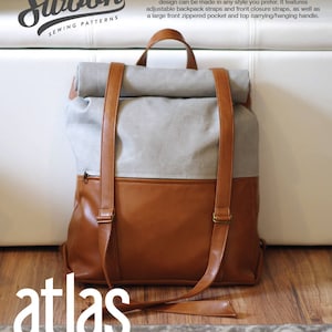 Könnte beinhalten: Ein brauner und grauer Rucksack mit Lederriemen und -akzenten. Die Tasche hat eine Reißverschlusstasche vorne und einen Tragegriff oben. Der Text "atlas Rucksack" ist auf der Vorderseite zu sehen. Die Tasche ist 35,5 cm breit und 12,7 cm tief.