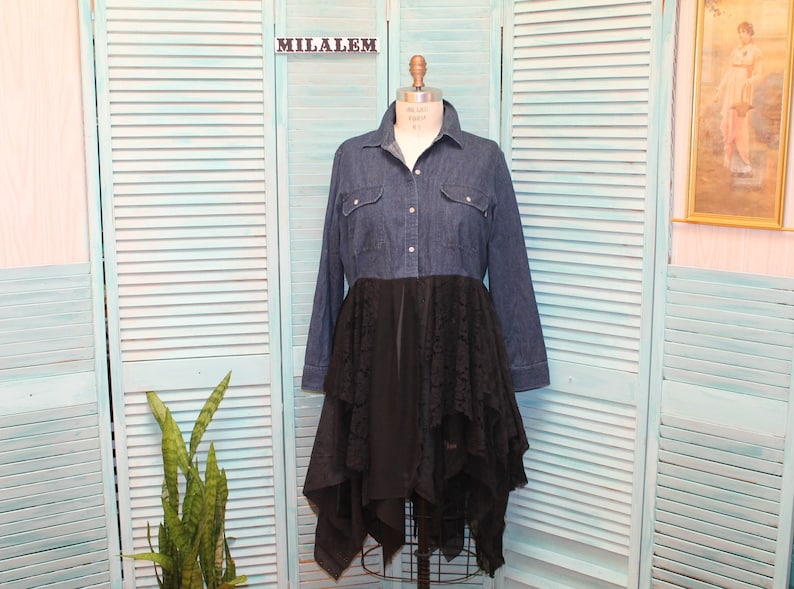 May include: A denim shirt dress with a black lace overlay. The dress has a long sleeve and a button-up front. The lace overlay is layered and asymmetrical.