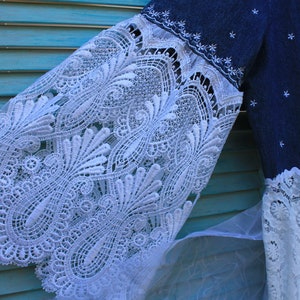May include: A blue denim dress with white lace trim. The lace is a delicate pattern with a floral design. The dress has a loose fit and a flowing skirt.