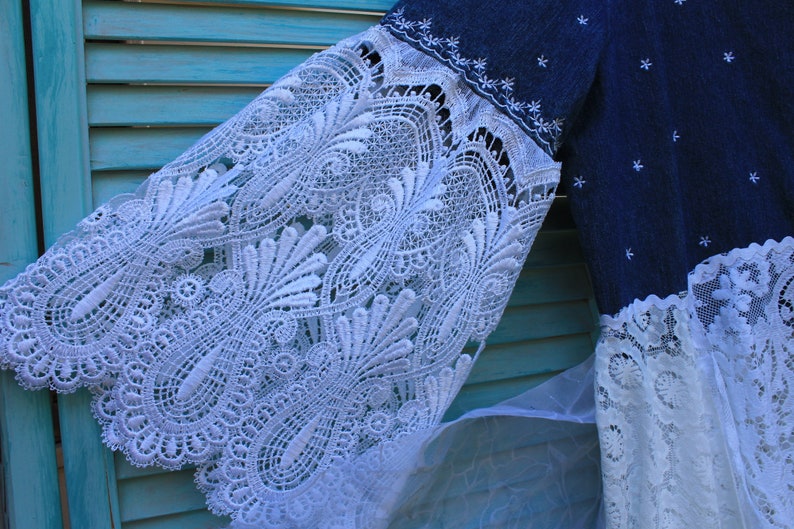 May include: A blue denim dress with white lace trim. The lace is a delicate pattern with a floral design. The dress has a loose fit and a flowing skirt.