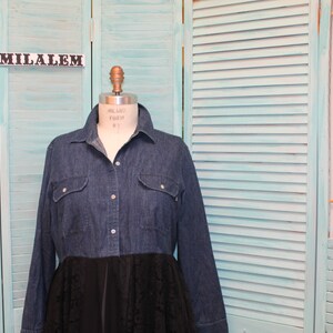 May include: A denim shirt dress with a black lace skirt overlay. The dress is on a mannequin in front of a light blue slatted wall.