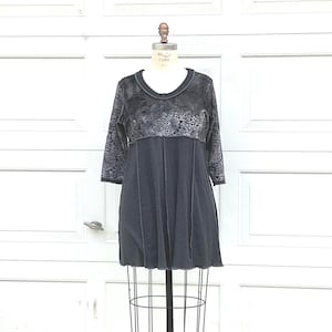 Könnte beinhalten: Dunkelgraues Kleid auf einer Draht-Schneiderpuppe. Das Kleid hat einen Rundhalsausschnitt und lange Ärmel mit einem floral gemusterten Oberteil. Der Rock ist dunklergrau und hat vertikale Nähte. Das Kleid ist ein lässiger Stil.