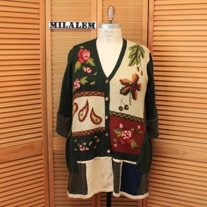 May include: A green, beige, and red cardigan with a patchwork design featuring floral and leaf motifs. The cardigan has a V-neck and button closure. The label "MILALEM" is visible on the left side of the image.