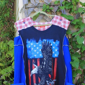 May include: A sleeveless top featuring a dark blue center panel with a graphic print of a bald eagle against a stylized American flag. The shoulders are accented with a red and white plaid fabric, and the sides are a solid bright blue color.