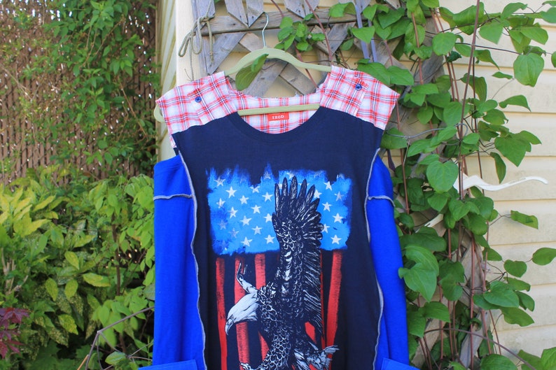 May include: A sleeveless top featuring a dark blue center panel with a graphic print of a bald eagle against a stylized American flag. The shoulders are accented with a red and white plaid fabric, and the sides are a solid bright blue color.