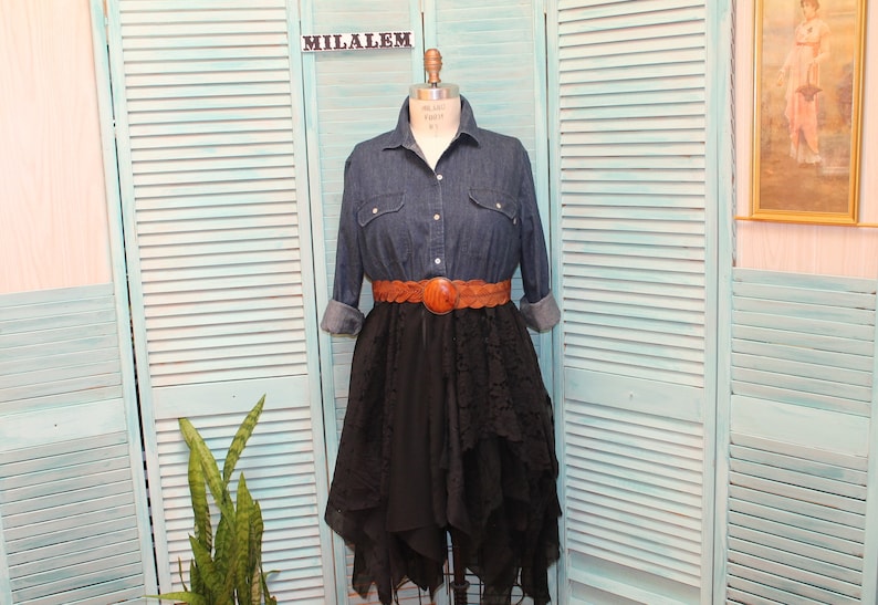 May include: A denim shirt with long sleeves and a brown leather belt over a black layered skirt. The skirt has a ruffled hem and is made of a sheer fabric.