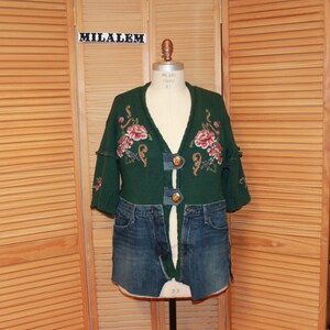 May include: A green cardigan with floral embroidery and gold buttons. The cardigan is paired with a denim skirt.