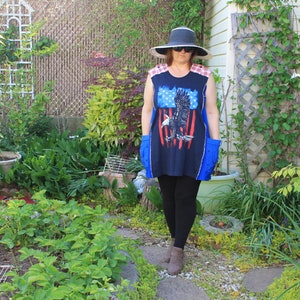 May include: A sleeveless navy blue tunic featuring a graphic of a bald eagle in front of red and white stripes, red and white plaid shoulder panels, and blue side pockets, paired with a wide-brimmed hat, sunglasses, and black leggings.