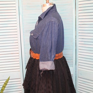 May include: A denim shirt with long sleeves and a brown leather belt. The shirt is worn over a black lace skirt.