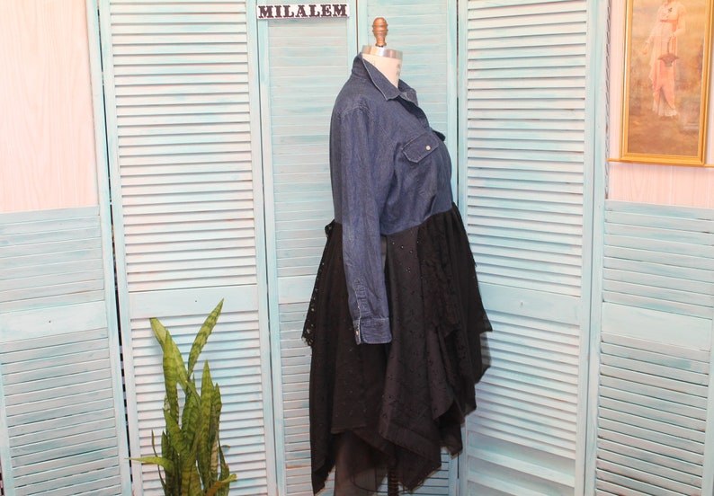 May include: A denim shirt dress with a black lace overlay. The dress has a long sleeve and a button-up front. The lace overlay is layered and asymmetrical.
