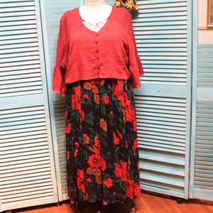 Puede incluir: Una blusa de lino roja con ribete de encaje blanco y una falda de estampado floral. La falda es negra con flores rojas, naranjas y verdes.
