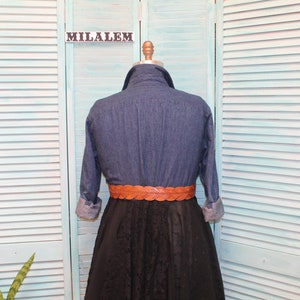 May include: A blue denim shirt with long sleeves and a brown braided belt. The shirt is on a mannequin in front of a light blue wooden slatted background.