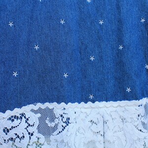 May include: A blue denim skirt with white embroidered stars and a white lace trim.