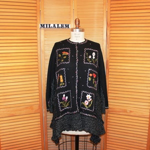 May include: Black cardigan sweater with a floral embroidery design. The cardigan has a ruffled hem and a button closure. The text "MILALEM" is visible on a tag.