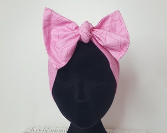 May include: Pink headband with a large bow, featuring a white swirl pattern. The headband is tied in a knot at the top of the bow.