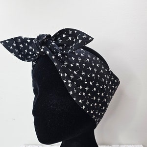May include: Black and white patterned headband with a white mushroom design. The headband is tied in a knot on top of a black mannequin head.